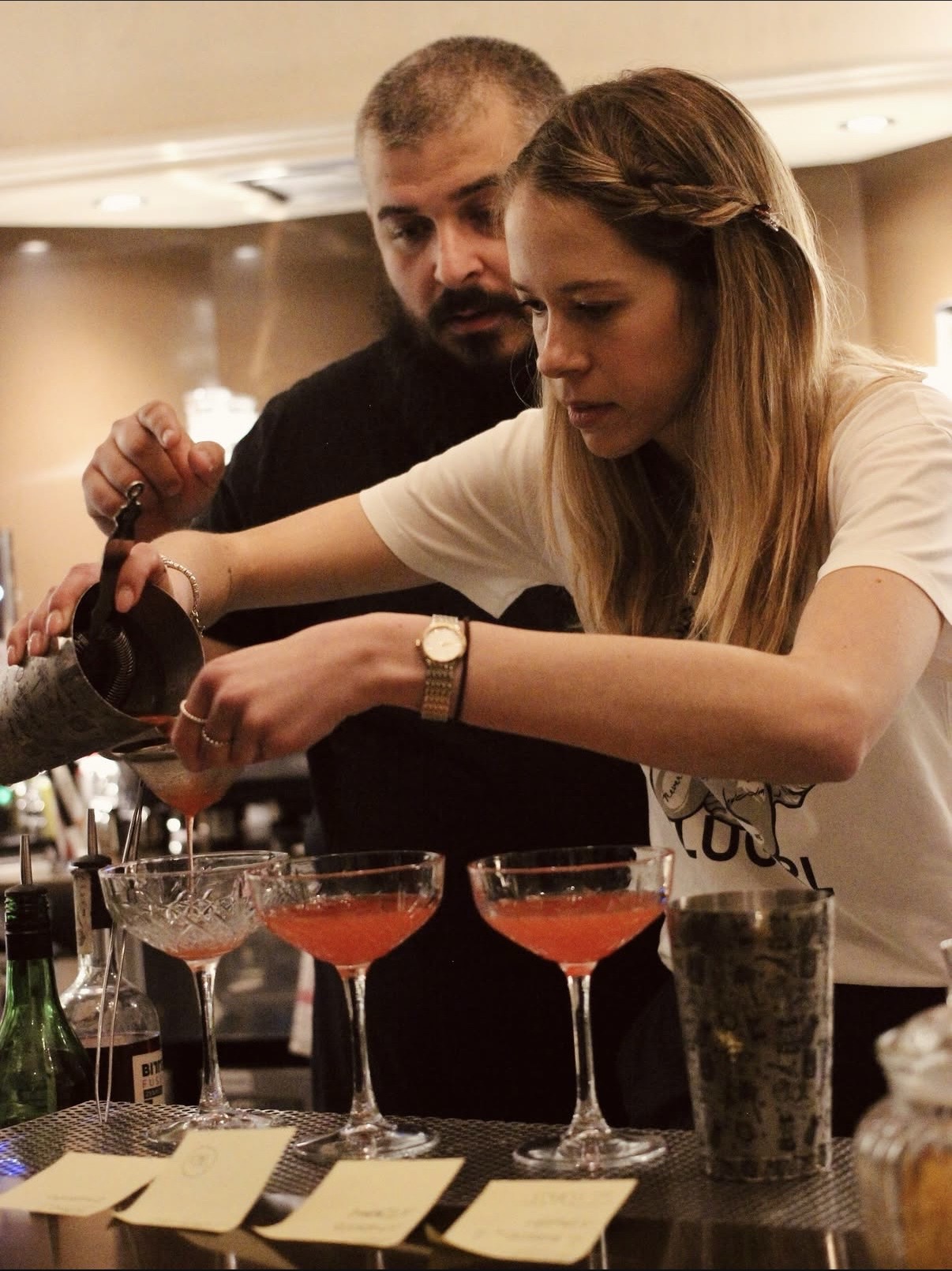 Bartender in formazione versa un cocktail rosa in coppe